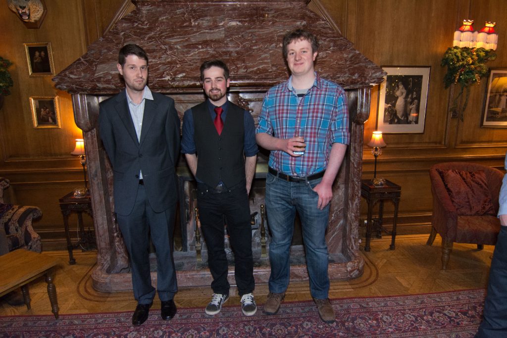 Three people at large fireplace at 2014 Christmas party