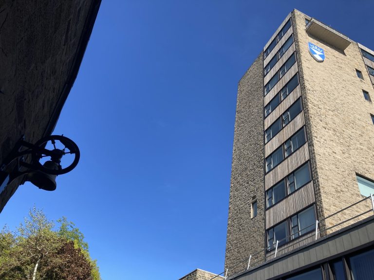 A photo taken from the ground looking up to the blue sky. The Tower Building at the University of Dundee is pictured on the right of the photo.