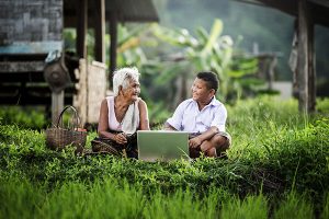 A boy and his grandmother collect data using a laptop in a lush and remote environment