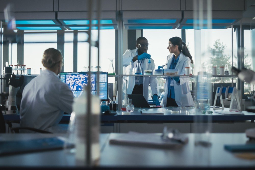 Two people in white lab coats looking at a beacon and one person sitting at a computer screen